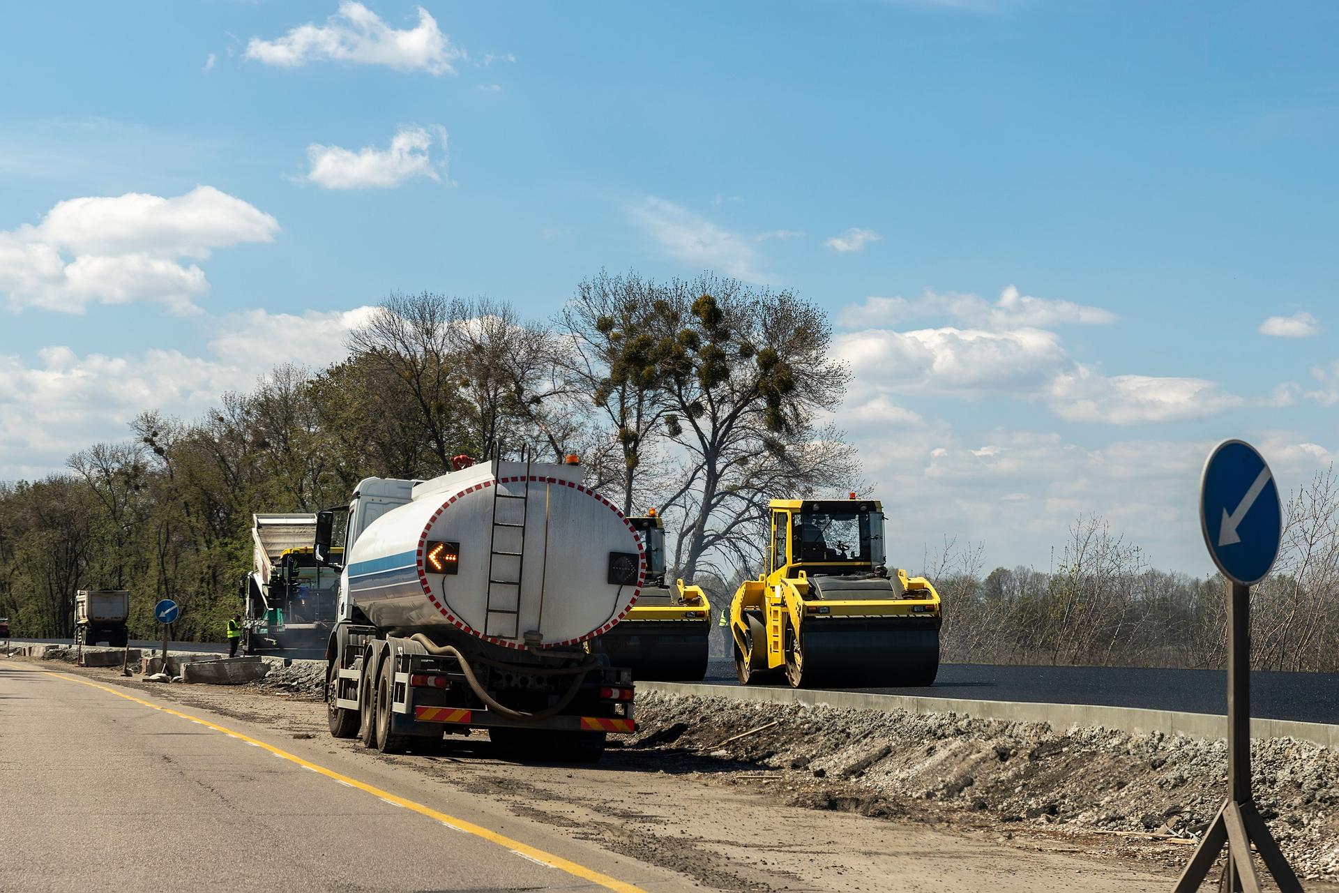 Highway intercity new road construction site with many heavy machinery steamroller, water tanker truck and paver tractor. Paving motorway road street works. Urban infrastructure development industry