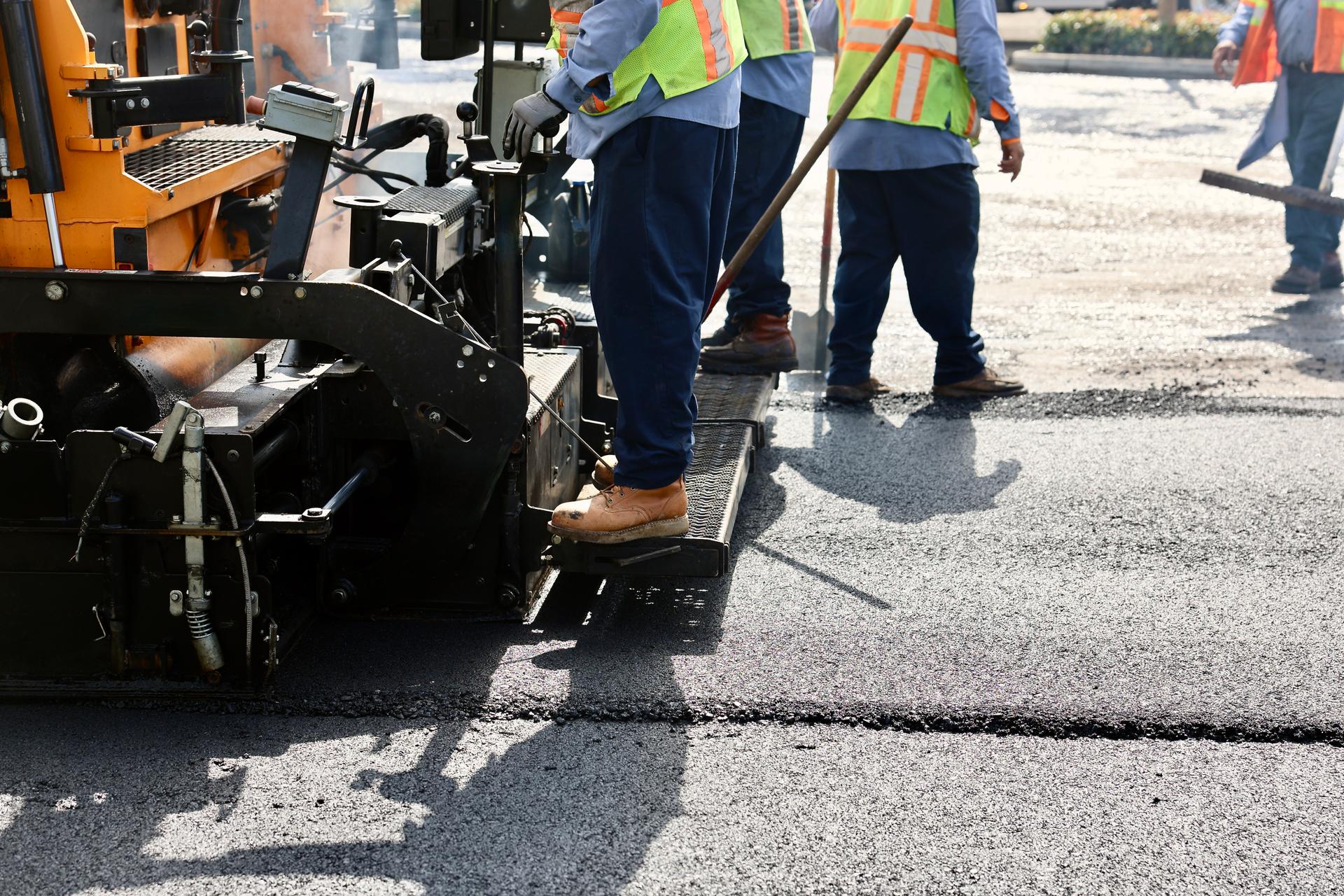 Blue collar workers operate the asphalt paving machine