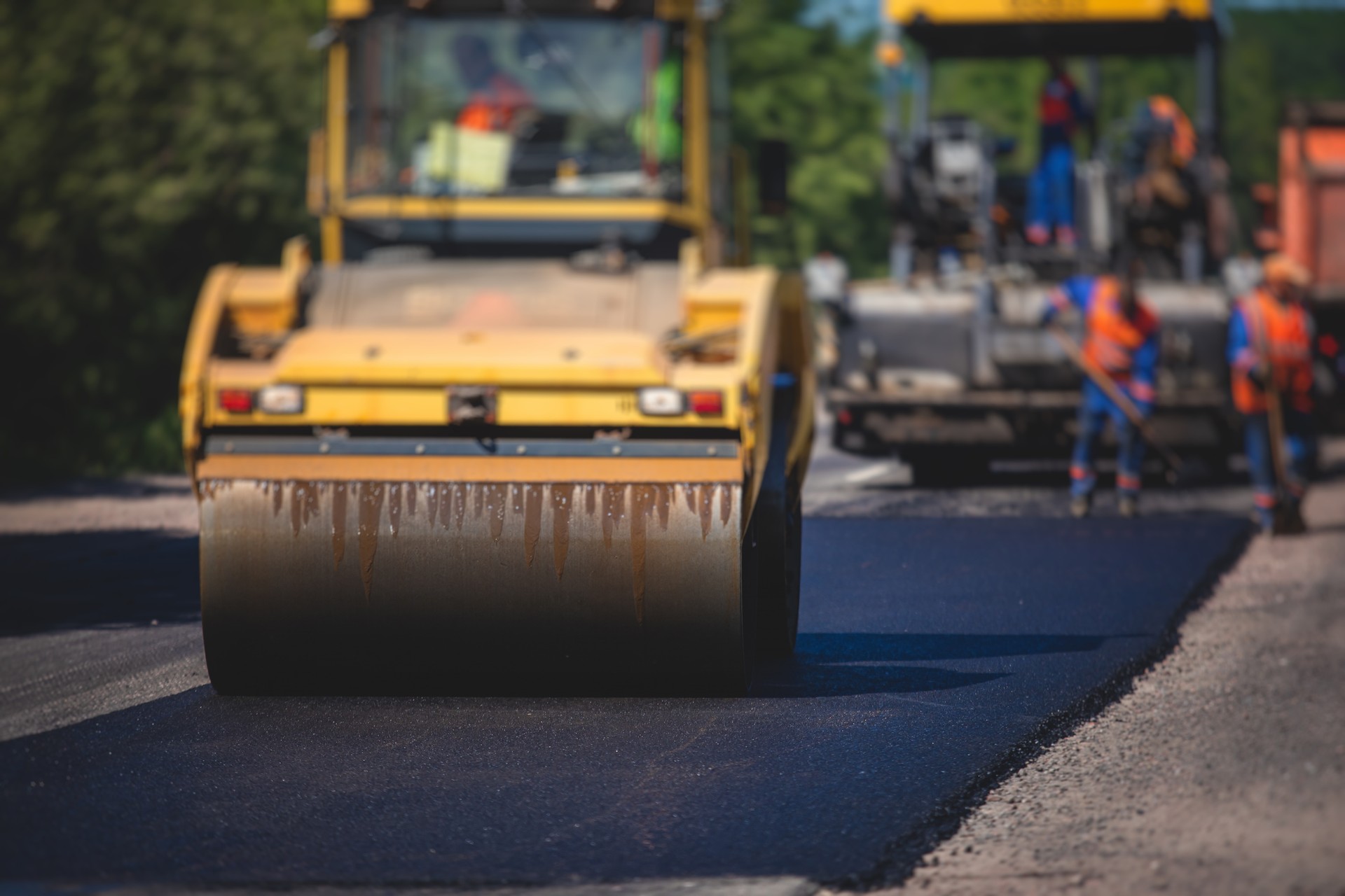 Process of asphalting and paving, asphalt paver machine and steam road roller during road construction and repairing works, workers working on the new road construction site, placing a layer in summer